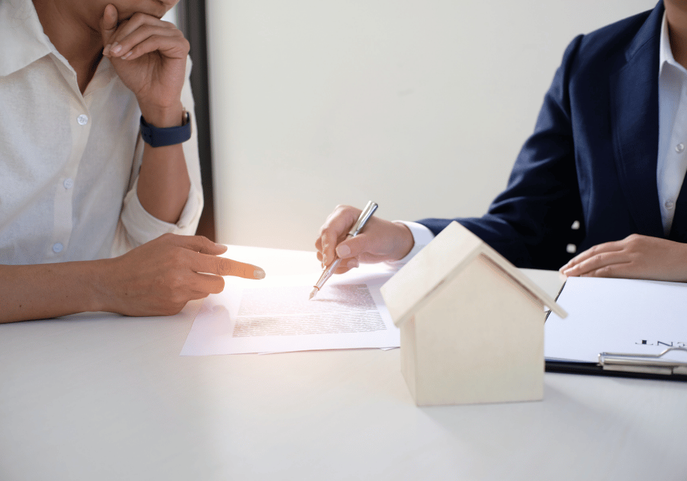 Two people reviewing an insurance policy and claim documents beside a model house